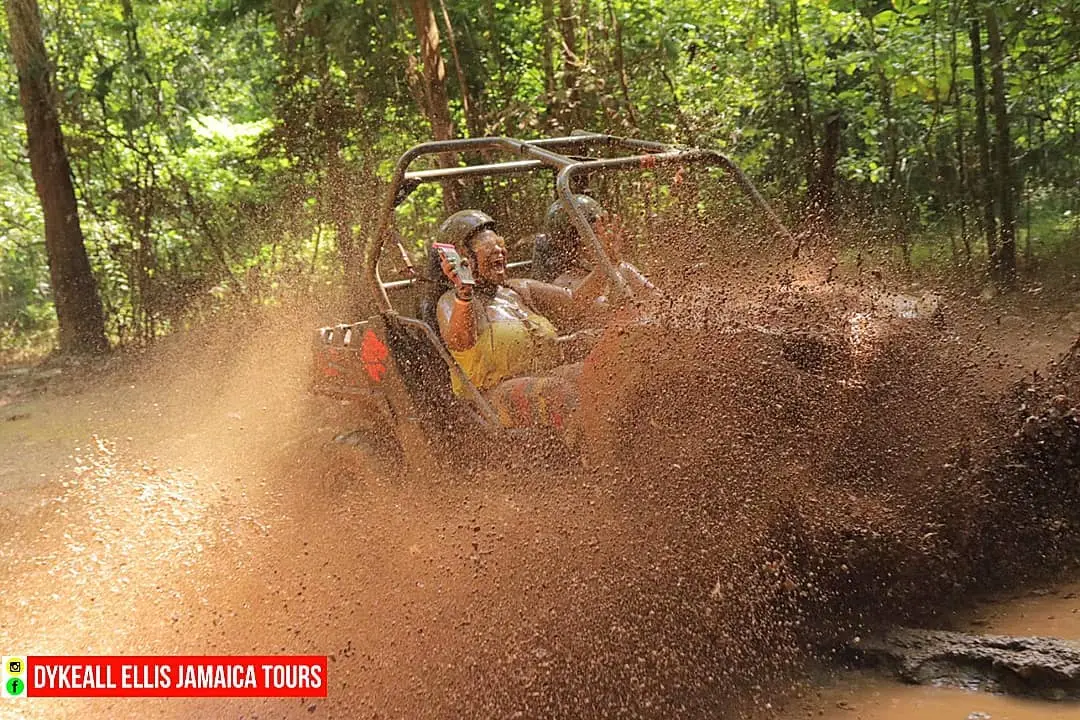 Guests in helmets riding a two-seat off-road buggy through a mud splash on a bush trail in Jamaica