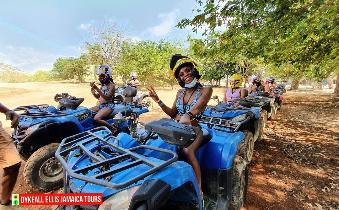 Guests in helmets sitting on a line of blue ATVs on a dirt trail in Jamaica