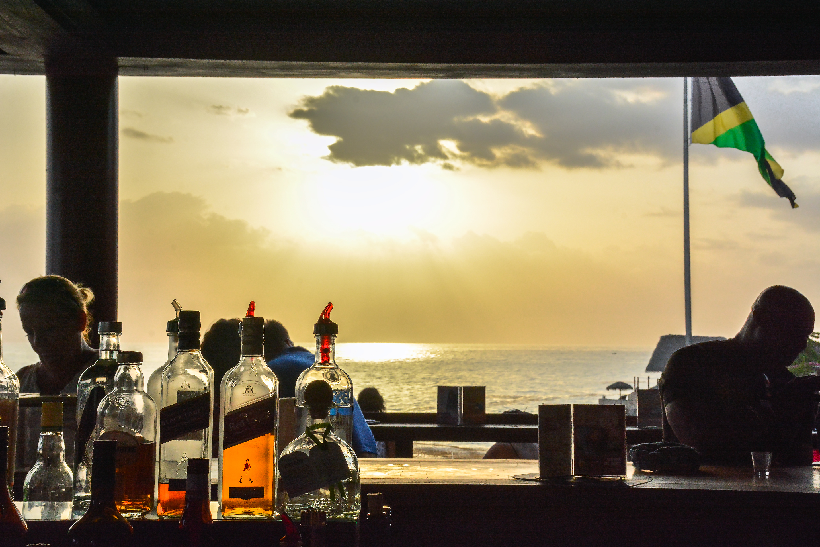 Sunset over the sea seen past the bottles on a Jamaican bar, with the flag flying