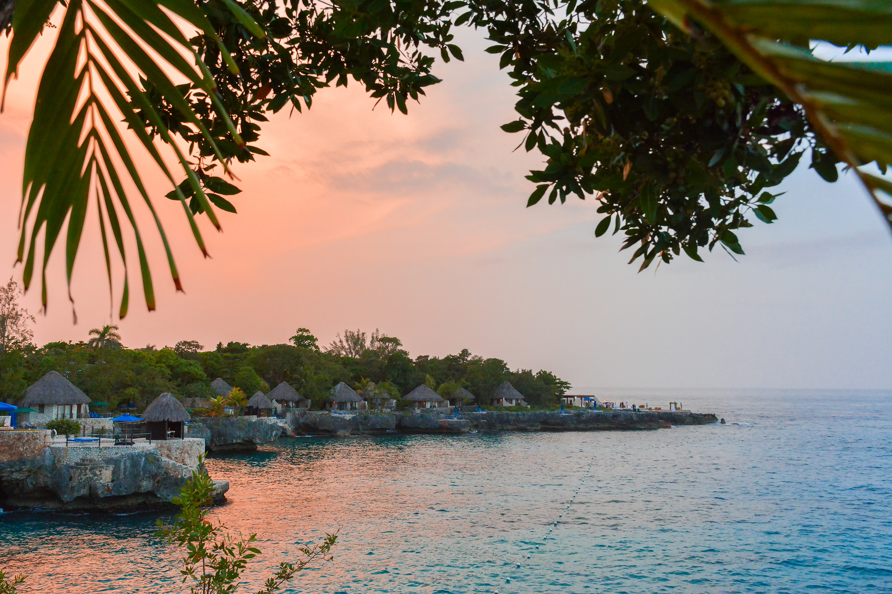 Dusk over the sea at Negril, framed by palms above a resort headland