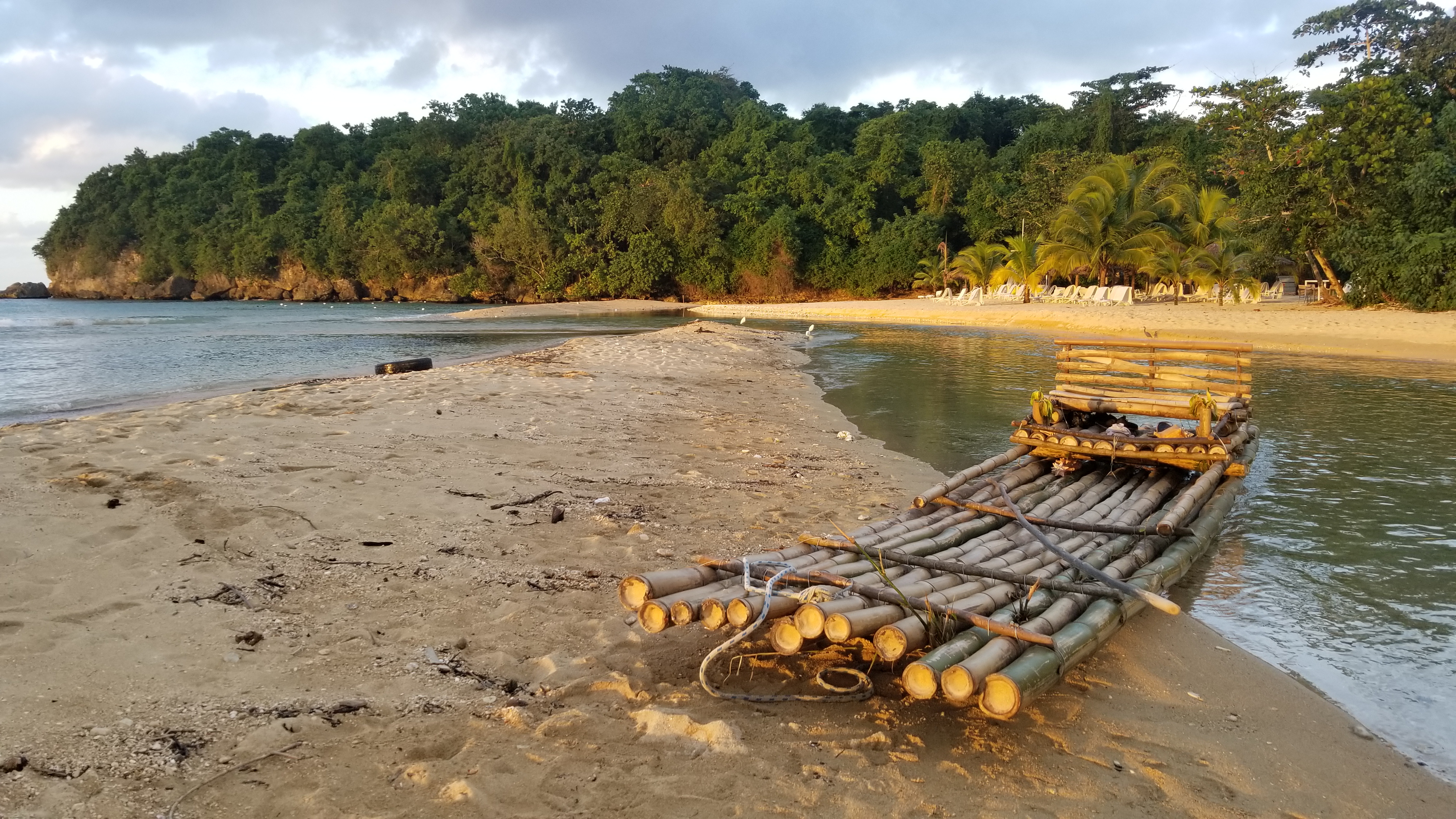 A bamboo raft pulled up on the sand of a quiet Jamaican beach in low afternoon sun